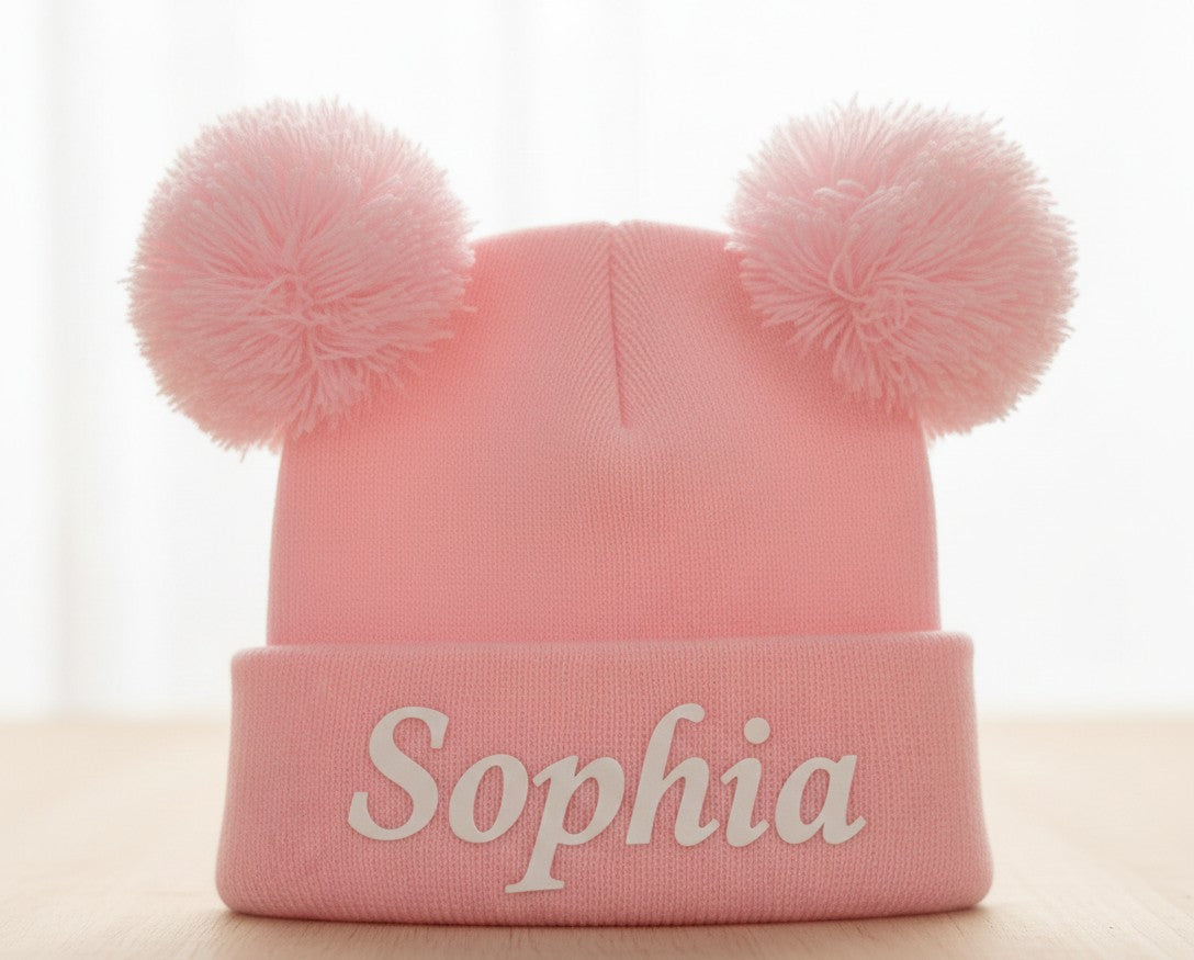 Pink personalised double pom pom baby beanie on white background