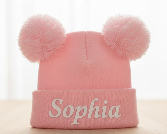 Pink personalised double pom pom baby beanie on white background