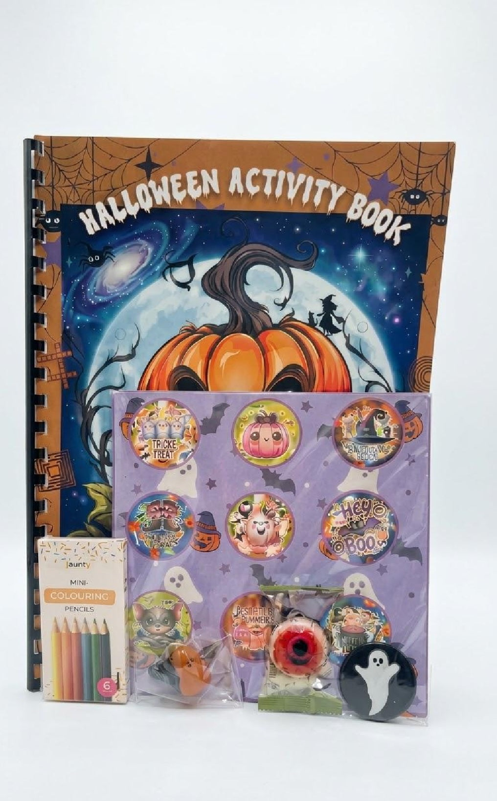 Halloween-themed activity book set with a spiral-bound book featuring a pumpkin and full moon cover, a purple sticker sheet with round Halloween stickers, a small pencil pack, and assorted small party accessories on a white background.